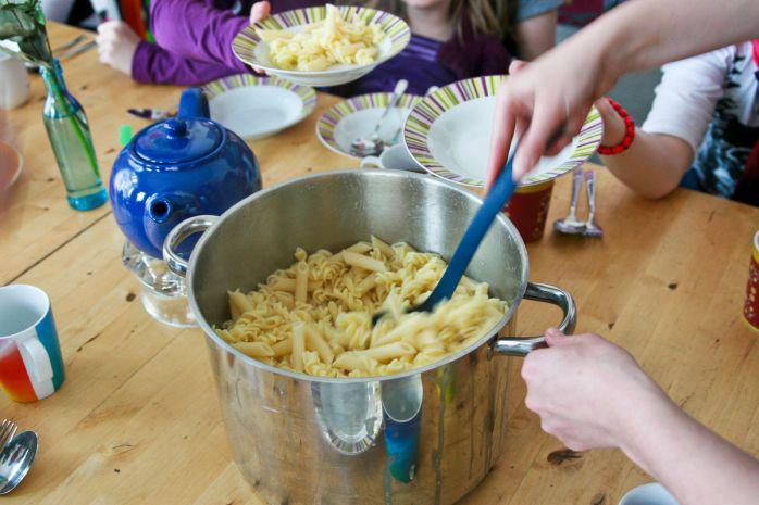 Eine Frau kocht Pasta, während die Kinder zusehen