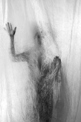 Eine Person steht hinter einem weißen Vorhang; ihre Silhouette ist als Schatten sichtbar und berührt den Stoff mit der Hand