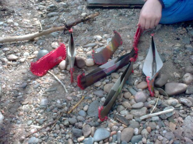 Ein Kind sitzt auf einem Kiesboden und hat sieben bunte Pappboote vor sich aufgestellt.