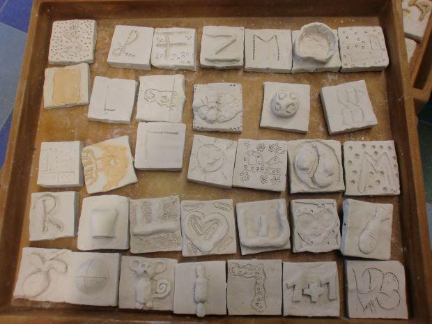 Mehrere Gipsstücke in kleinen Quadraten, einige mit eingravierten Buchstaben, andere in Formen wie Herz, Fisch und Affe.