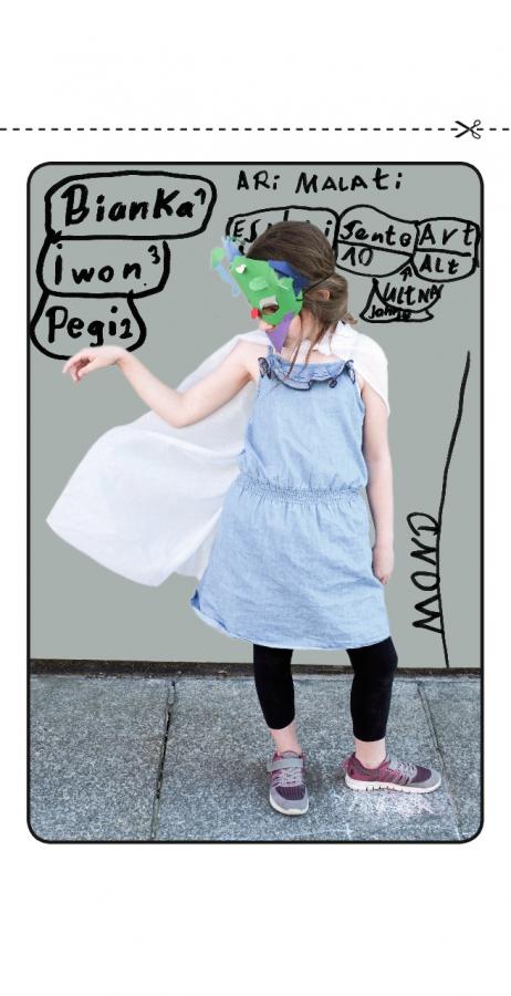 Ein kleines Mädchen steht, trägt eine Papiermaske und einen weißen Umhang auf dem Rücken, hinter ihr eine Wand mit den Namen ihrer Freunde