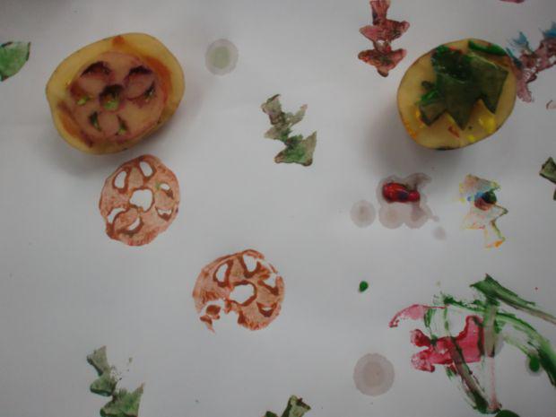 Zwei Kartoffelhälften mit Baum- und Kreisform werden auf Papier gestempelt, die Muster in Rot und Grün sichtbar.