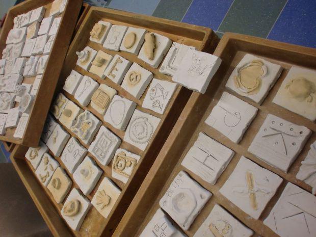 Drei Holzkisten mit kleinen Gipsstücken, teils mit Herzen, Kamera, Hand und Buchstaben graviert