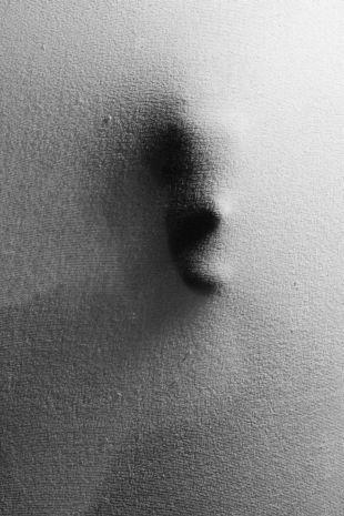 Eine Person steht hinter einem Vorhang und drückt ihr Gesicht von hinten gegen den Stoff.