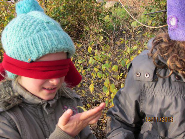 Zwei kleine Mädchen tragen Wintermützen und Jacken, eines von ihnen hat die Augen mit einem roten Tuch bedeckt.