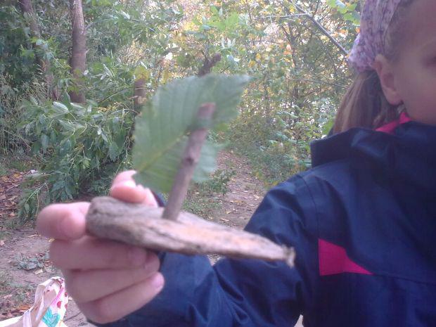 Ein Mädchen steht im Wald und hält mit einer Hand ein Stück Holz in Form eines Bootes