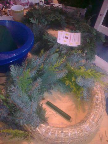 Ein Tisch mit zwei Weihnachtskränzen, einer vollständig geschmückt und der andere noch unvollständig