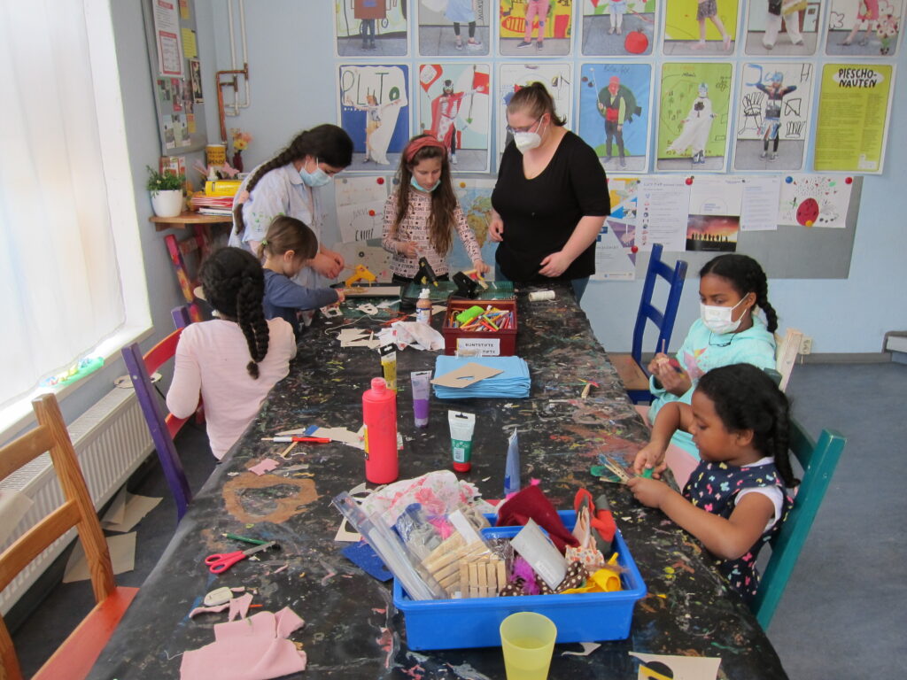 Fünf Mädchen und zwei Frauen basteln Papierarbeiten an einem Tisch