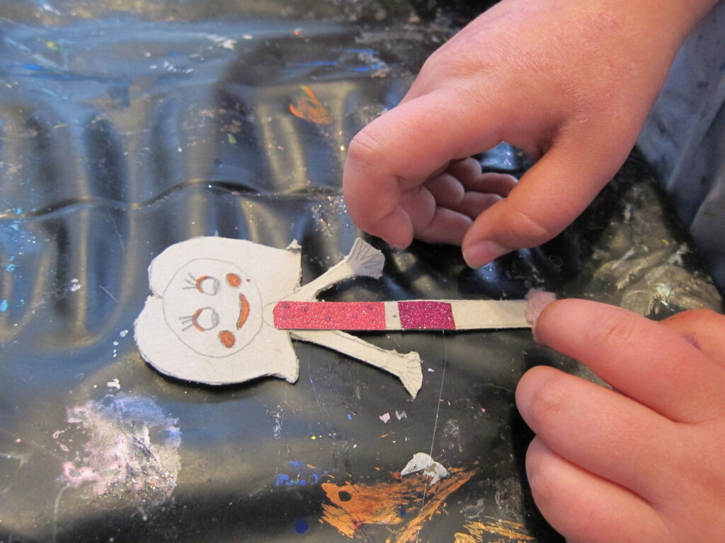 Die Hände eines Kindes basteln eine Papierpuppe in Form eines Mädchens